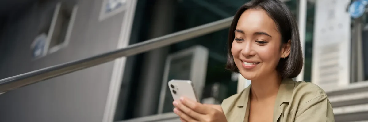 Portrait of asian girl takes selfie on mobile phone. Korean woman smiling, video chat on smartphone app while sits outside on stairs.